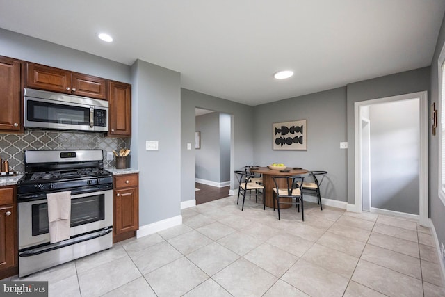 kitchen with appliances with stainless steel finishes, backsplash, baseboards, light tile patterned floors, and light stone countertops