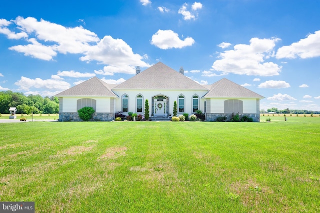 french provincial home featuring stone siding, a front yard, and roof with shingles