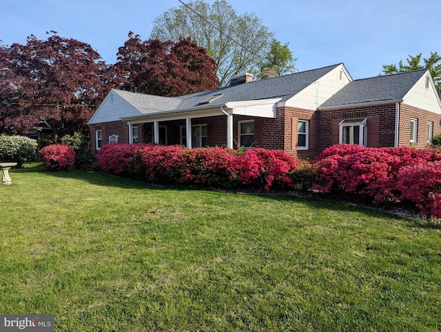 view of side of home featuring a lawn, brick siding, a shingled roof, and a chimney
