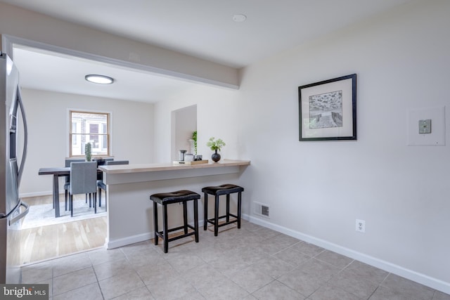 7923 Karl Rd, Alexandria, VA 22308 - kitchen with stainless steel fridge, a kitchen breakfast bar, baseboards, a peninsula, and light tile patterned flooring