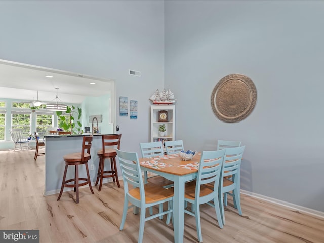 dining space featuring light wood-style flooring, baseboards, and a high ceiling