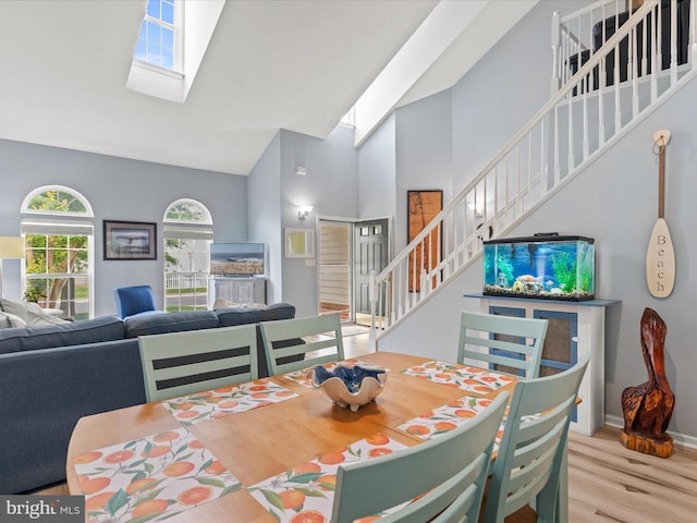 dining room featuring high vaulted ceiling, stairway, a skylight, wood finished floors, and baseboards