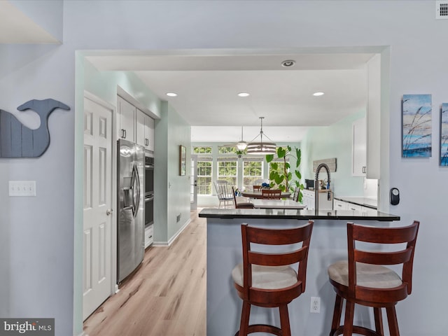 kitchen with light wood-style flooring, a peninsula, dark countertops, a breakfast bar area, and white cabinets