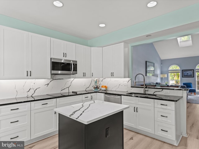 kitchen with stainless steel appliances, a sink, a peninsula, open floor plan, and a skylight