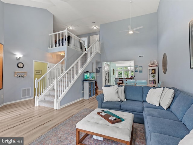 living area with high vaulted ceiling, stairs, wood finished floors, a ceiling fan, and baseboards