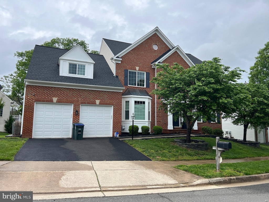 traditional home with driveway, brick siding, an attached garage, a front lawn, and a shingled roof
