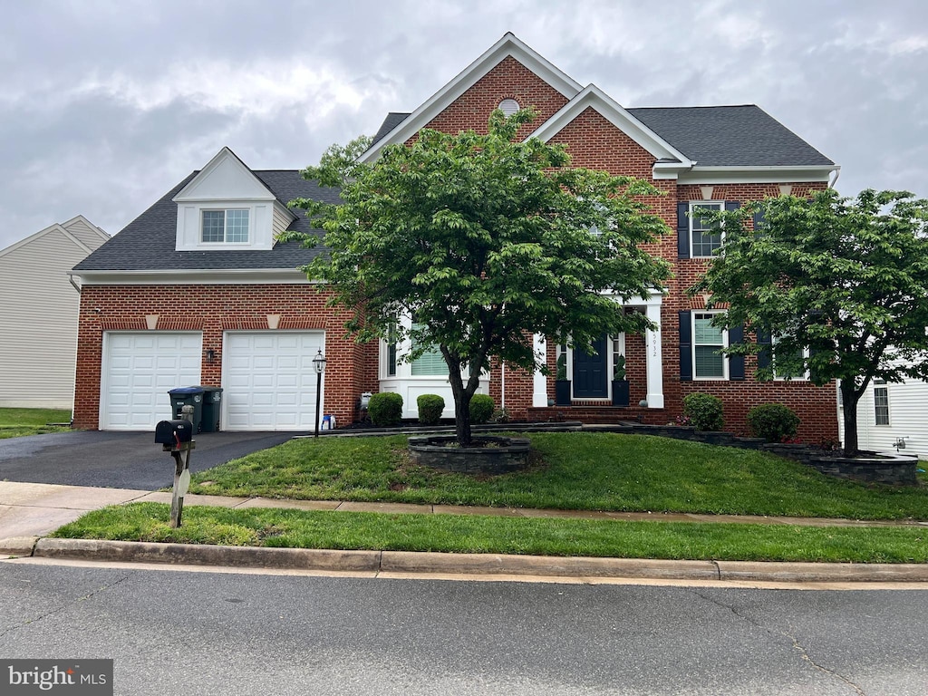 view of front of house with asphalt driveway, a front lawn, brick siding, an attached garage, and a shingled roof