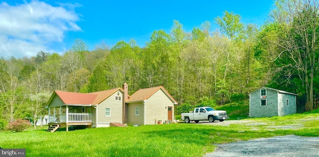 view of side of home featuring a wooded view, a lawn, and gravel driveway