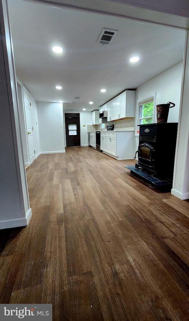 living area featuring wood finished floors, baseboards, recessed lighting, and a wood stove