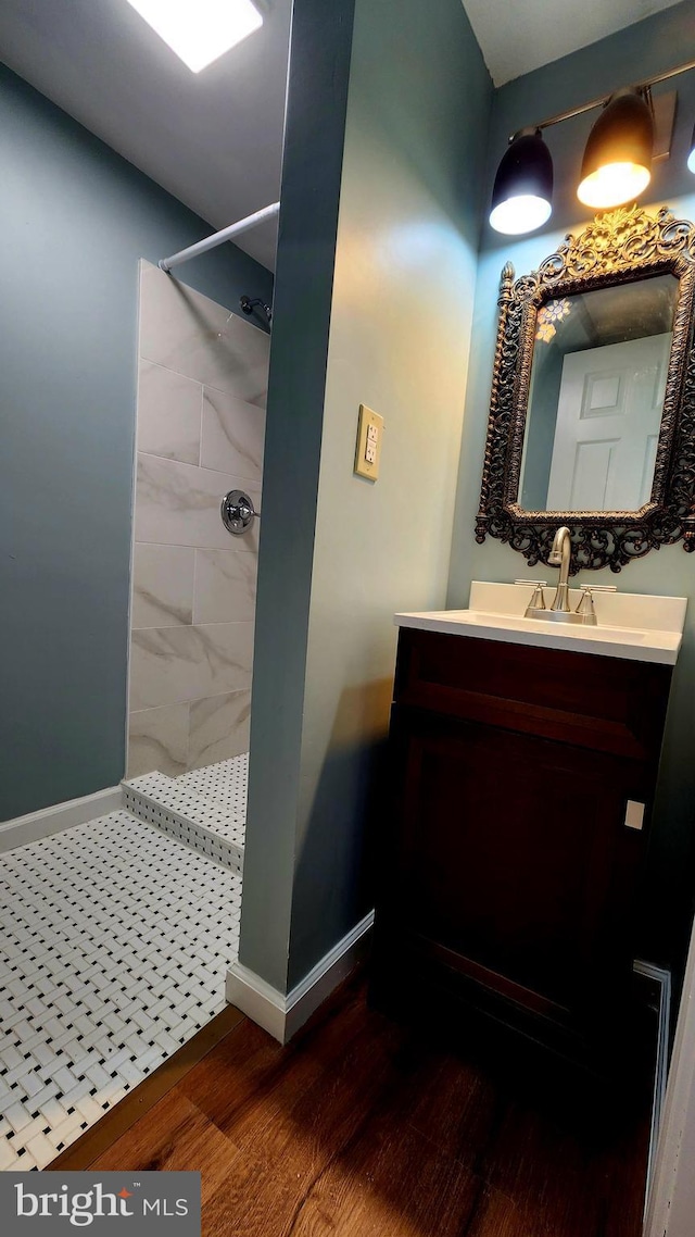 full bath featuring wood finished floors, tiled shower, vanity, and baseboards