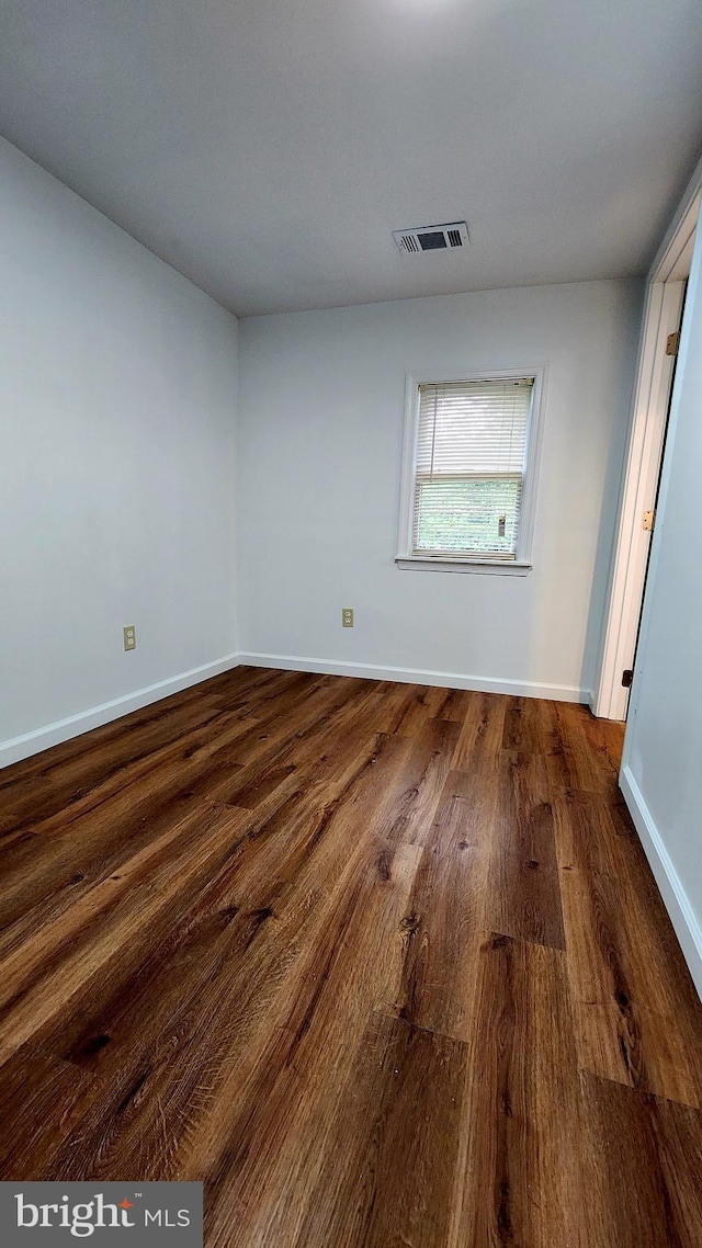spare room featuring dark wood-type flooring and baseboards