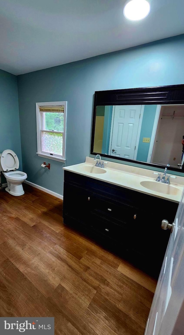 bathroom with wood finished floors, double vanity, baseboards, and toilet