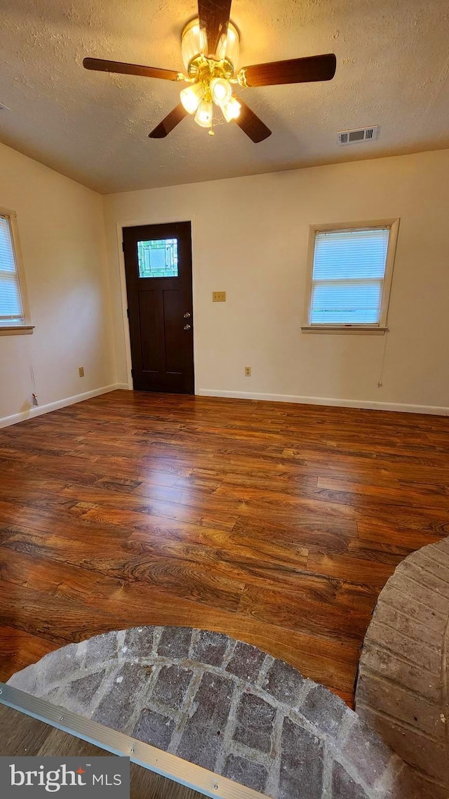 foyer entrance with a textured ceiling, wood finished floors, ceiling fan, healthy amount of natural light, and baseboards