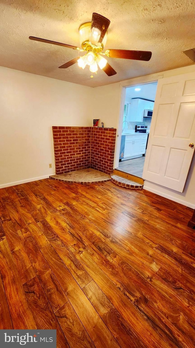 unfurnished room with a textured ceiling, wood finished floors, a ceiling fan, and baseboards