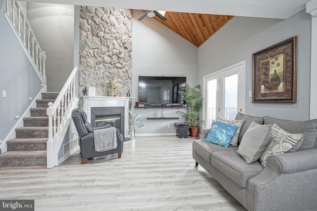 living room with stairway, wood ceiling, wood finished floors, a ceiling fan, and a glass covered fireplace