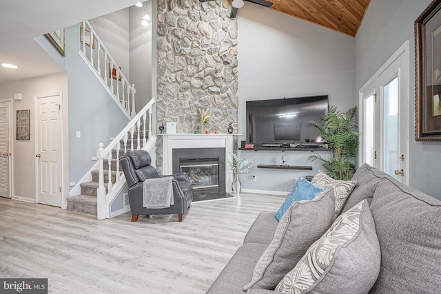 living room featuring stairway, wood finished floors, a glass covered fireplace, baseboards, and high vaulted ceiling