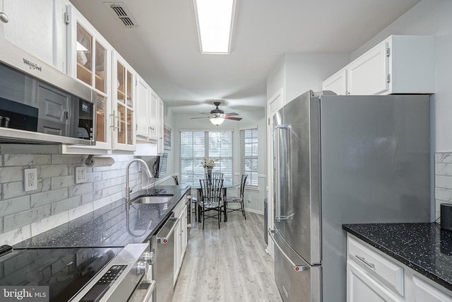 kitchen with a sink, appliances with stainless steel finishes, backsplash, white cabinets, and dark stone counters