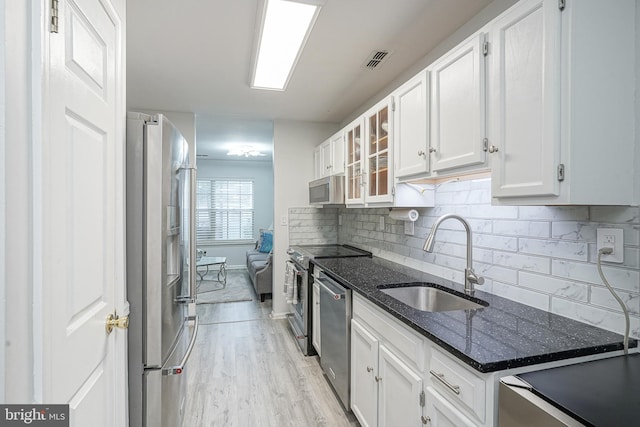 kitchen with a sink, appliances with stainless steel finishes, light wood-type flooring, white cabinets, and tasteful backsplash