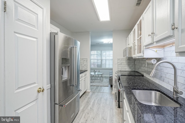 kitchen with appliances with stainless steel finishes, a sink, white cabinetry, light wood-type flooring, and glass insert cabinets