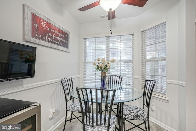dining area with a ceiling fan, wine cooler, wood finished floors, and baseboards