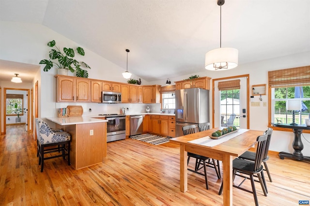 kitchen featuring stainless steel appliances, a peninsula, lofted ceiling, light wood-style flooring, and light countertops