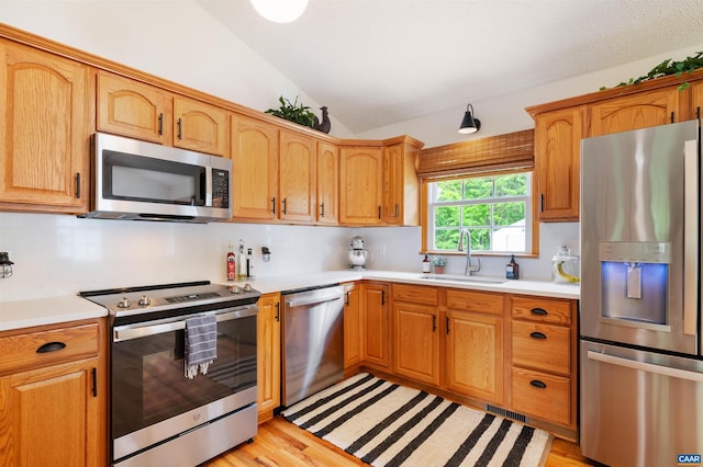 kitchen featuring appliances with stainless steel finishes, a sink, lofted ceiling, light countertops, and light wood finished floors