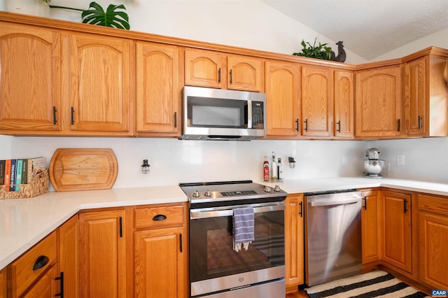 kitchen featuring appliances with stainless steel finishes, lofted ceiling, light countertops, and brown cabinets
