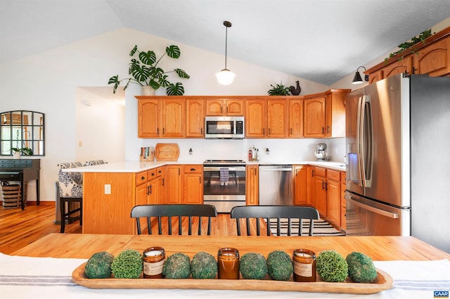 kitchen with stainless steel appliances, vaulted ceiling, a peninsula, light countertops, and a breakfast bar