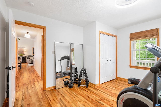exercise area featuring light wood-style flooring, baseboards, and a textured ceiling