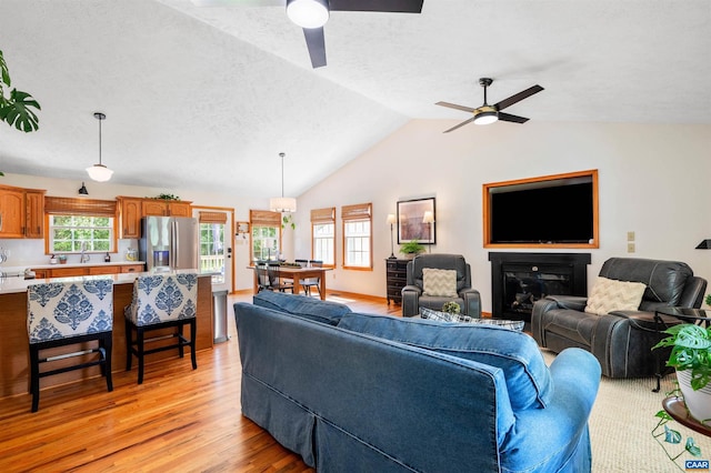 living room with ceiling fan, light wood-style floors, plenty of natural light, vaulted ceiling, and a textured ceiling