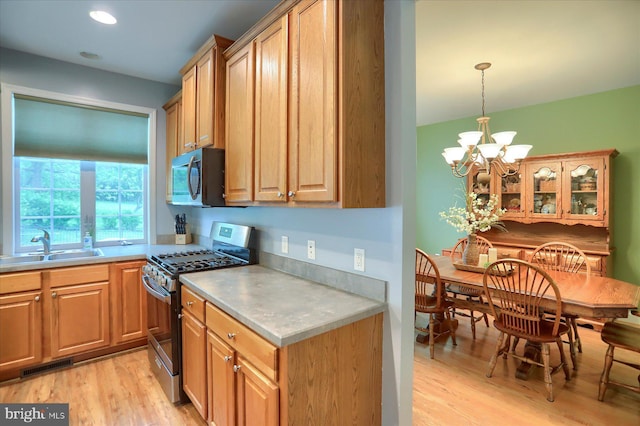 kitchen featuring appliances with stainless steel finishes, light wood-style flooring, a sink, a chandelier, and light countertops