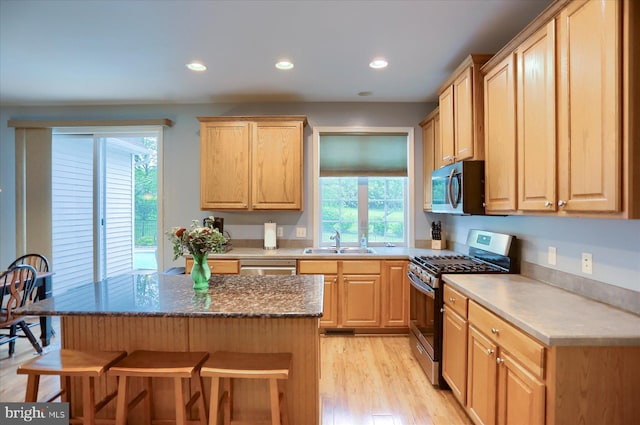 kitchen with stainless steel appliances, a sink, a kitchen breakfast bar, light brown cabinets, and recessed lighting