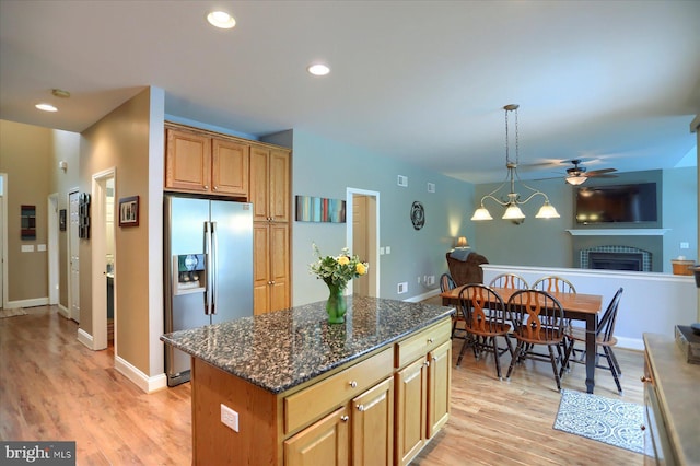 kitchen featuring stainless steel fridge, ceiling fan, light wood-style floors, a fireplace, and dark stone counters