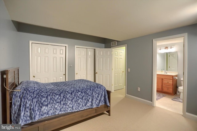 bedroom featuring multiple closets, light colored carpet, connected bathroom, and baseboards