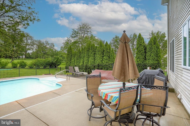 view of swimming pool featuring a patio, fence, and view of wooded area
