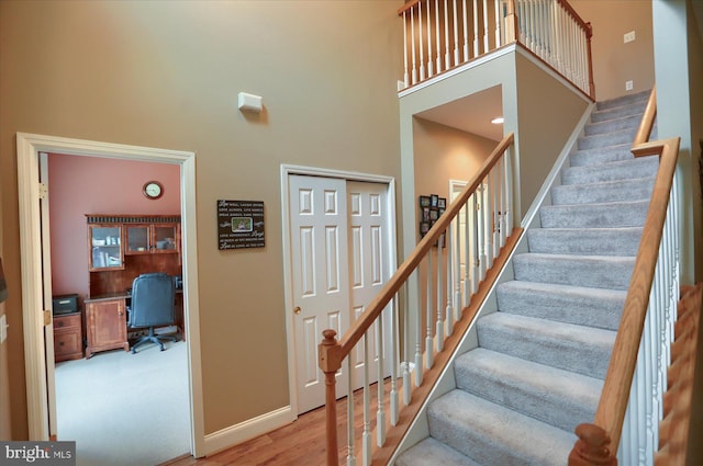 stairs with a towering ceiling, baseboards, and wood finished floors