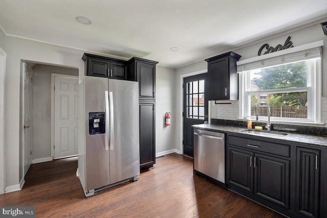 kitchen featuring stainless steel appliances, a sink, dark wood-type flooring, backsplash, and baseboards