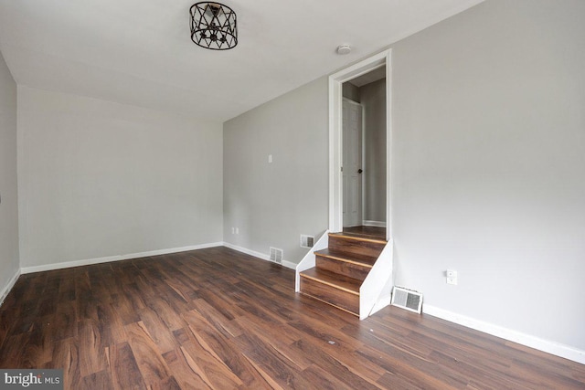 spare room featuring dark wood-type flooring, stairway, and baseboards