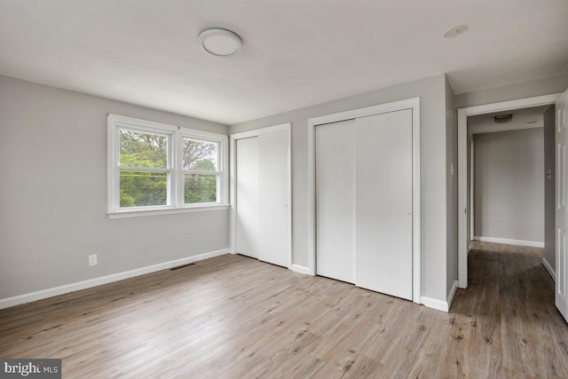 unfurnished bedroom featuring multiple closets, wood finished floors, and baseboards