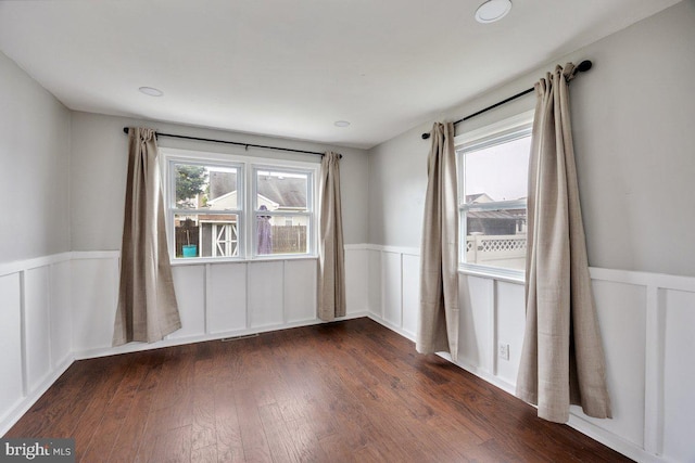 unfurnished room featuring a wainscoted wall, dark wood-type flooring, and a decorative wall