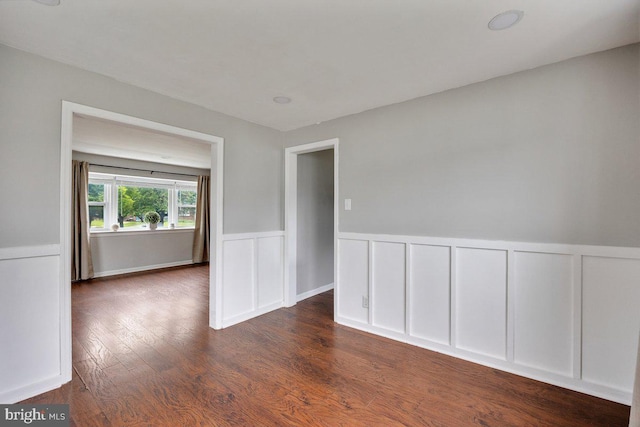 spare room with wainscoting, dark wood-style floors, and a decorative wall