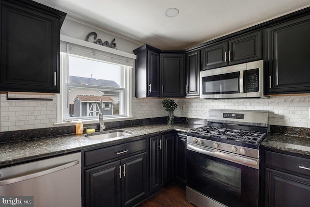kitchen featuring stainless steel appliances, dark cabinetry, a sink, and backsplash