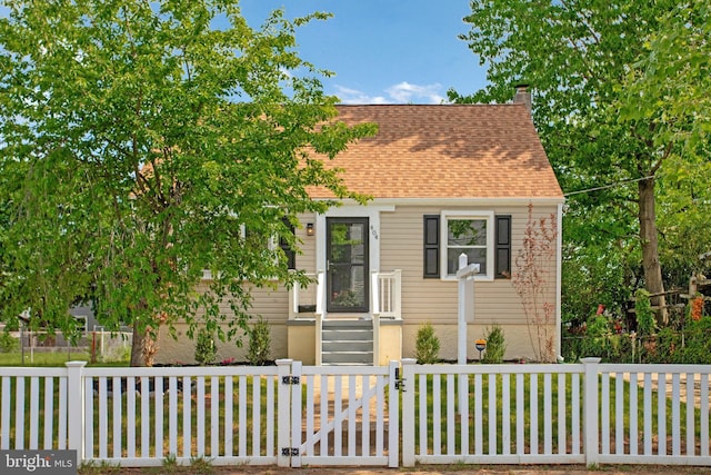 cape cod house featuring a shingled roof, a chimney, and a fenced front yard