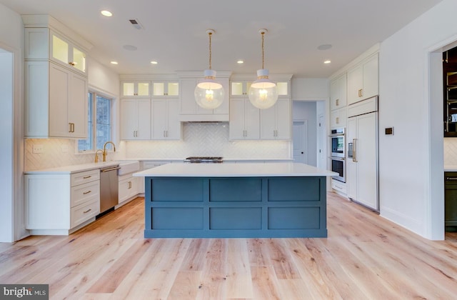 kitchen featuring appliances with stainless steel finishes, light countertops, white cabinetry, a kitchen island, and backsplash