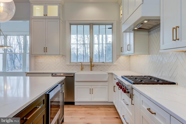 kitchen with a sink, custom exhaust hood, light stone counters, and white cabinets