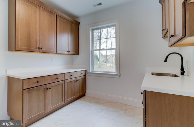 kitchen featuring a sink, light marble finish flooring, light countertops, and baseboards
