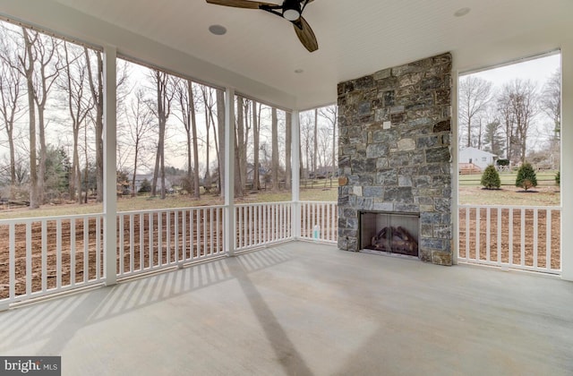 unfurnished sunroom featuring an outdoor stone fireplace and a ceiling fan