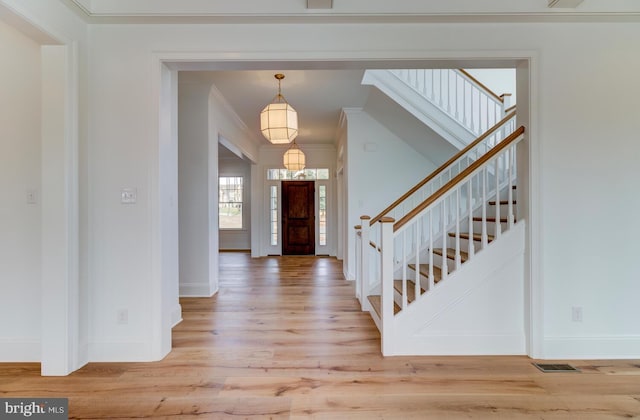 entrance foyer featuring crown molding, light wood-style flooring, stairs, baseboards, and a chandelier