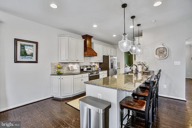kitchen with appliances with stainless steel finishes, a sink, custom exhaust hood, a kitchen breakfast bar, and dark wood-style floors
