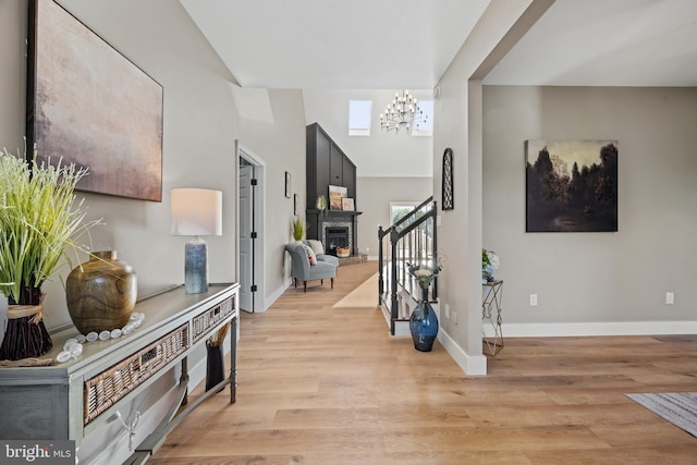 foyer featuring a chandelier, light wood finished floors, baseboards, and a fireplace with raised hearth